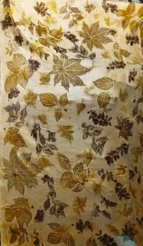 Kain ecoprint krem dengan cetakan daun berwarna cokelat dan kuning keemasan
