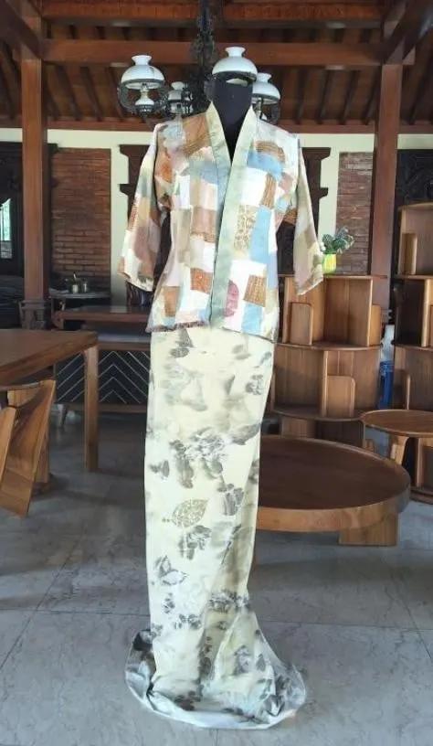 Manekin mengenakan outer perca warna pastel dan rok panjang ecoprint krem bermotif daun di pendopo kayu