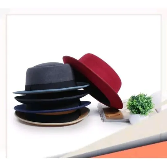 Tumpukan topi bermahkota datar abu-abu, hitam dan biru dongker dengan satu topi merah bersandar