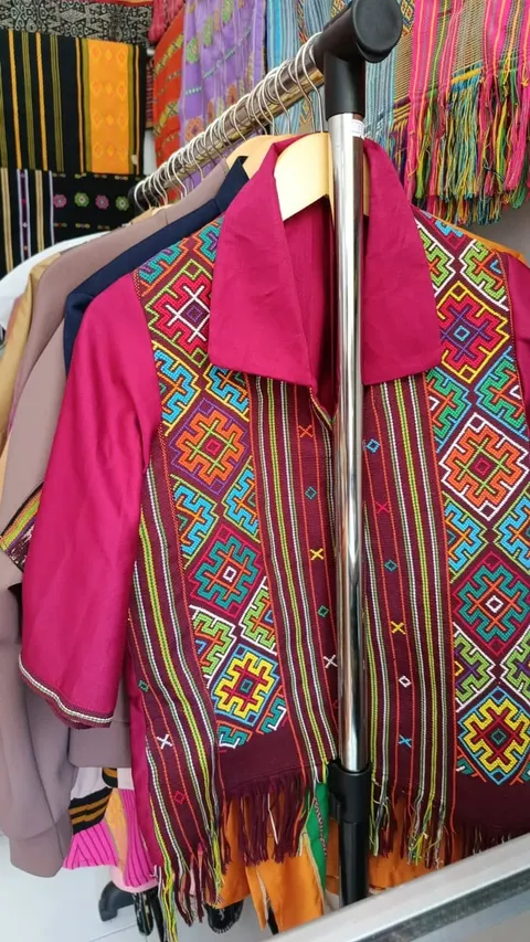 Kemeja merah muda berpanel tenun motif warna-warni berumbai, tergantung di rak pakaian