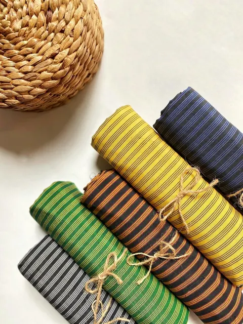 Gulungan kain lurik kuning, biru, hijau, cokelat dan abu-abu diikat tali rami di samping tatakan anyaman