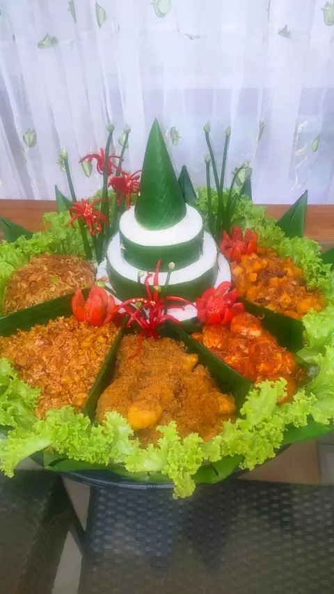 Tumpeng nasi putih berbalut daun pisang dengan hiasan cabai merah, dikelilingi mi, telur balado, lauk lain dan selada