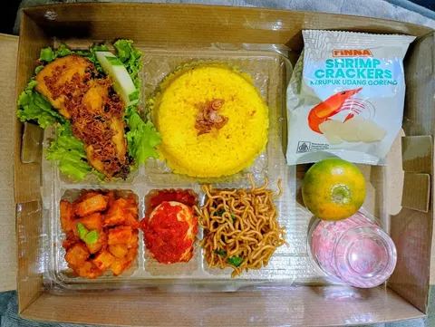 Nasi kotak berisi nasi kuning, ayam goreng, sambal goreng kentang, telur balado, mi goreng, kerupuk udang dan jeruk