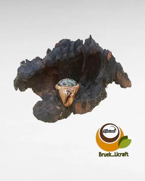 Cincin bermata batu hijau berbintik dengan gagang dari batok kelapa, diletakkan pada potongan kayu hitam