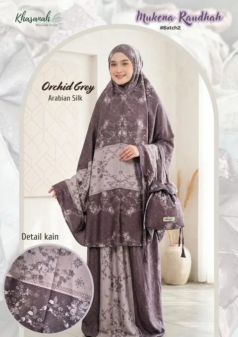 Model memakai mukena ungu keabuan motif bunga dengan tas serut senada, berlabel Mukena Raudhah Orchid Grey