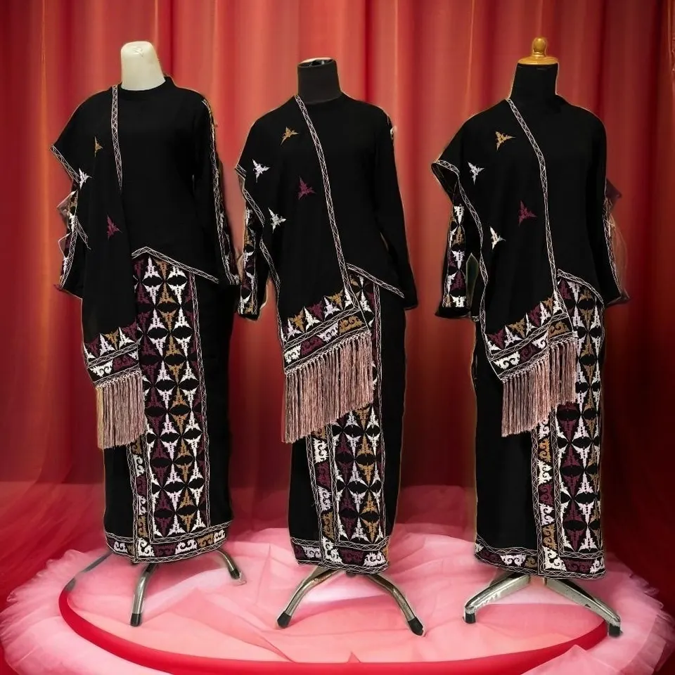 Tiga manekin bersetelan hitam dengan selendang berumbai dan rok berbordir motif Aceh warna ungu, putih, dan emas