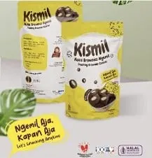 Dua kemasan standing pouch kuning Kismil berisi kukis brownies bulat, dengan daun hijau di latar