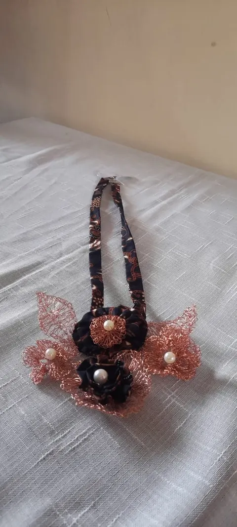 Kalung tali kain batik cokelat tua dengan bunga dan daun dari kawat tembaga serta mutiara di atas kain abu