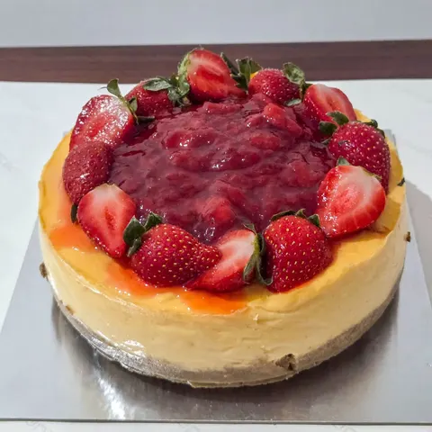 Cheesecake bulat dengan topping saus stroberi dan potongan stroberi segar di sekelilingnya