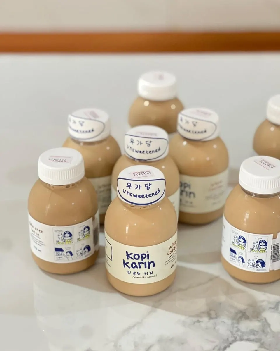 Botol plastik kopi susu Kopi Karin bertutup putih dengan stiker Unsweetened di atas meja marmer