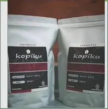 Dua kemasan kopi putih berlabel hitam Kopiku dengan pita merah bertuliskan Arabica Gayo
