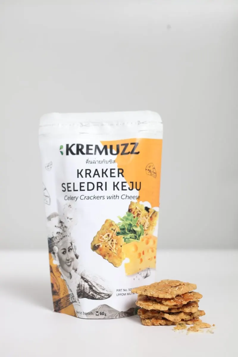 Kemasan pouch Kremuzz Kraker Seledri Keju dengan tumpukan kraker tipis di depannya