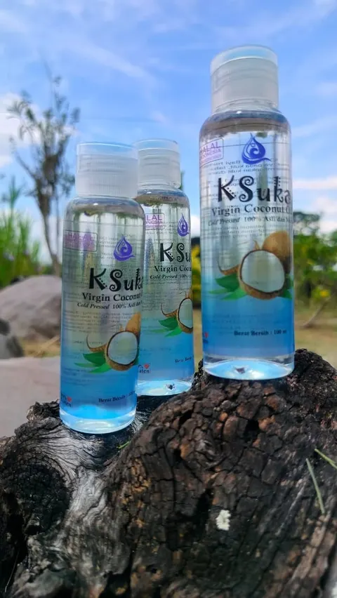 Tiga botol plastik KSuka Virgin Coconut Oil 100 ml di atas batang kayu dengan latar langit biru