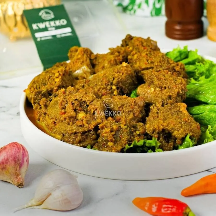 Potongan bebek berbumbu rempah kecokelatan di piring putih dengan selada, bawang merah, bawang putih, dan cabai