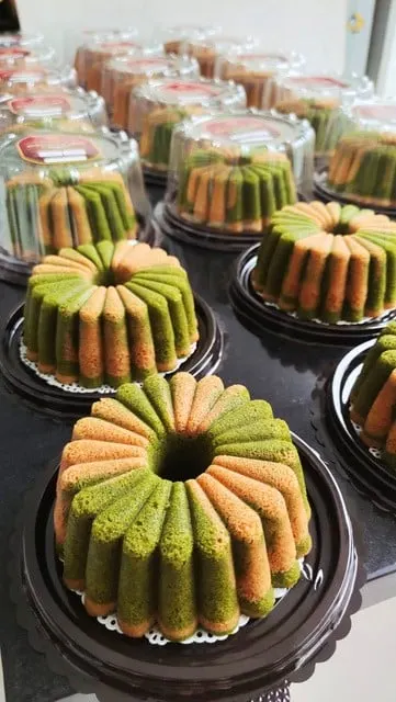 Bolu berbentuk cincin bergerigi berwarna hijau dan cokelat muda di atas alas hitam