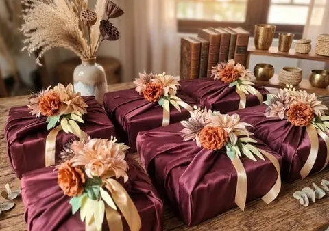 Enam hantaran terbungkus kain satin merah marun dengan hiasan bunga peach dan pita krem di atas meja kayu