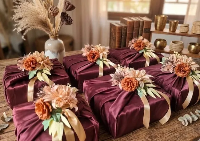 Enam hantaran terbungkus kain satin merah marun dengan hiasan bunga peach dan pita krem di atas meja kayu