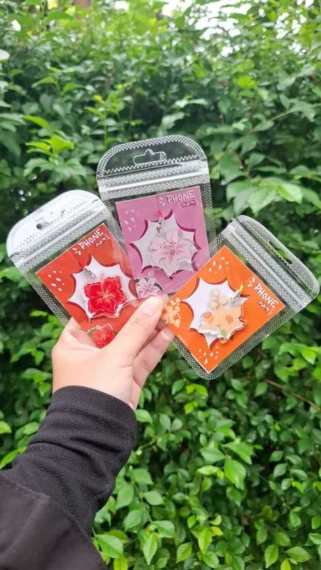 Tangan memegang tiga phone charm akrilik bergambar bunga dalam kemasan plastik zip berkartu Phone Charm