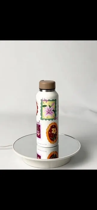 Botol minum putih bertutup cokelat dengan ilustrasi bunga bergaya perangko di atas meja putar