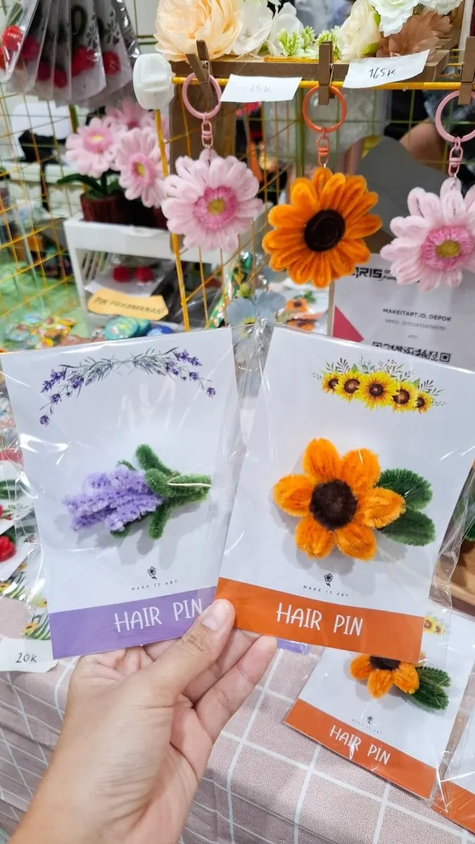 Tangan memegang jepit rambut bunga lavender dan bunga matahari dari bulu kawat pada kartu Hair Pin di stan bazar
