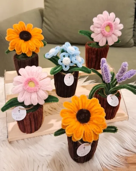 Beberapa pot kecil berisi bunga matahari, gerbera, lavender dan bunga biru dari bulu kawat di atas meja