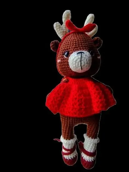 Boneka rajut rusa cokelat bergaun merah dengan pita merah di kepala, berlatar hitam