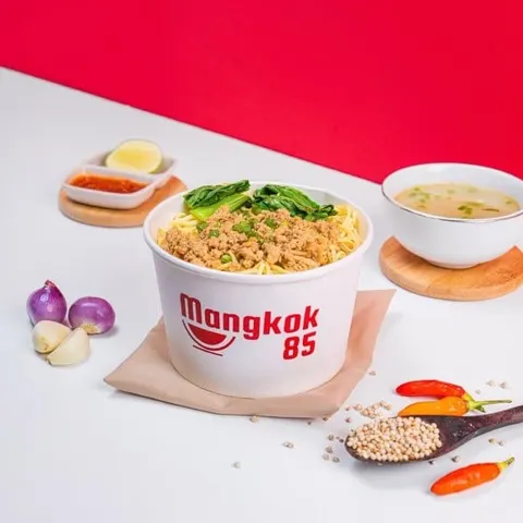 Mi ayam dengan sawi dalam mangkuk kertas Mangkok 85, ditemani semangkuk kuah dan sambal di meja putih