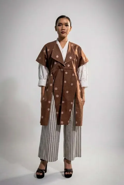 Model memakai luaran cokelat bermotif bunga putih di atas kemeja putih dan celana kulot bergaris