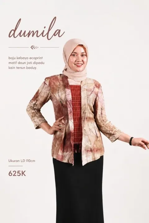 Model berhijab memakai kebaya ecoprint motif daun nuansa cokelat kemerahan dan rok hitam, bertuliskan dumila