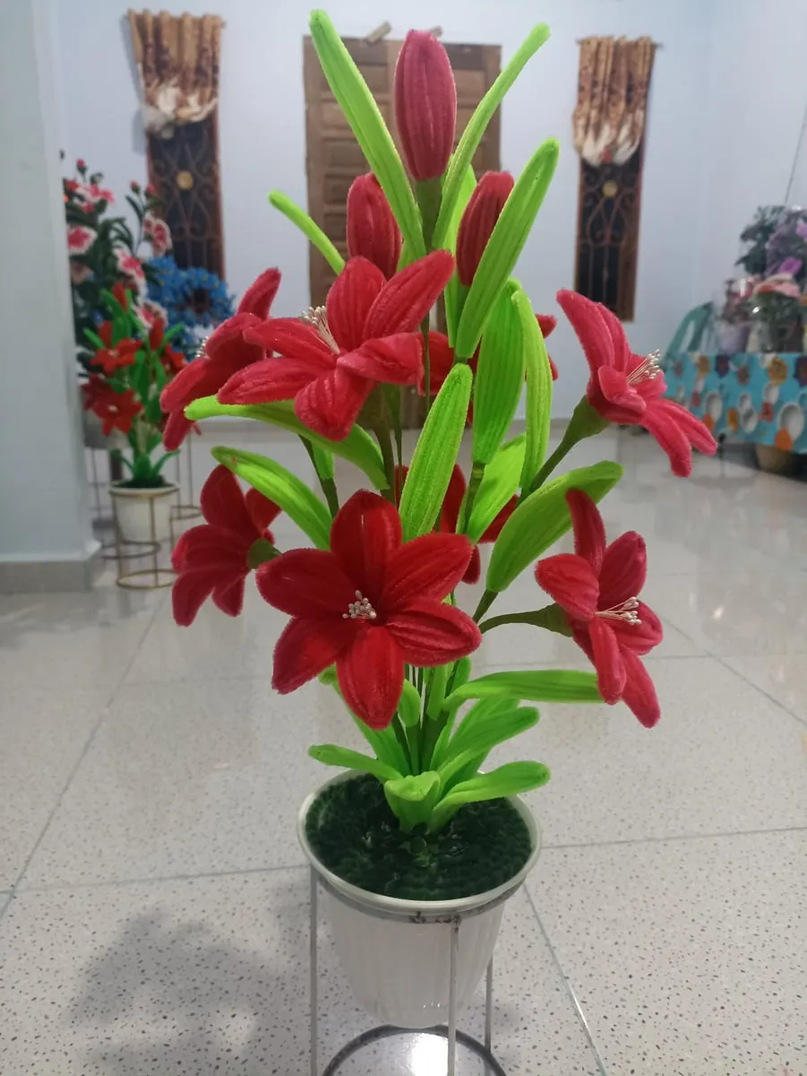 Rangkaian bunga lili kawat bulu merah dengan daun hijau dalam pot perak di lantai ruangan