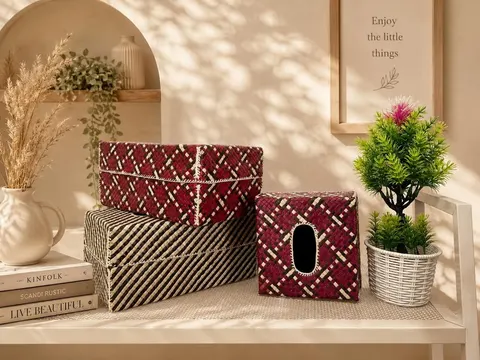 Dua kotak bertutup dan satu kotak tisu dari anyaman pandan motif merah marun dan hitam krem di atas meja putih