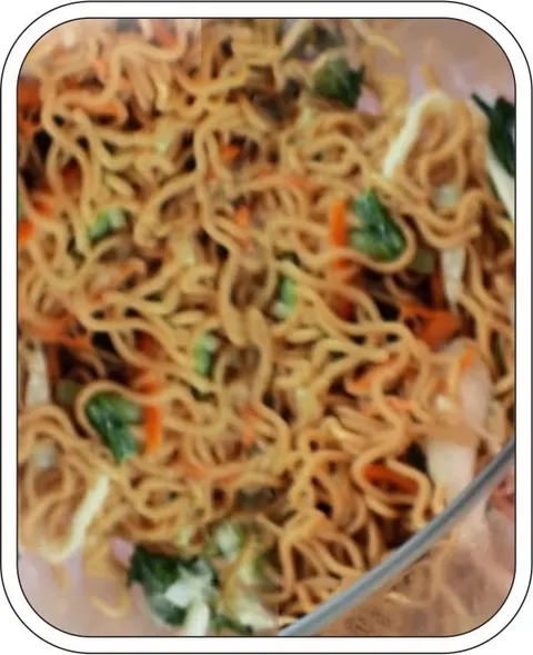 Mi goreng dengan potongan sawi hijau dan wortel dalam wadah kaca