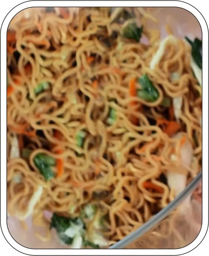 Mi goreng dengan potongan sawi hijau dan wortel dalam wadah kaca