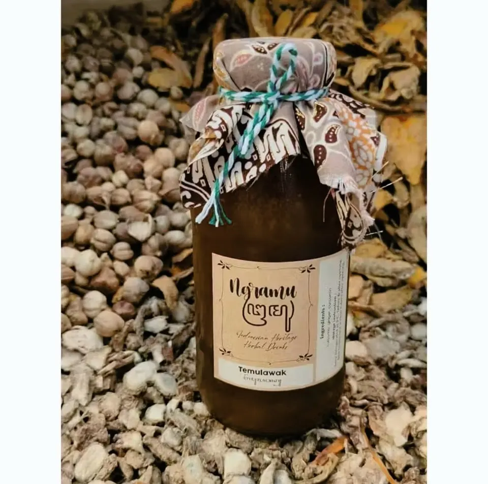 Botol kaca jamu Temulawak berlabel Ngramu dengan tutup kain batik, di atas tumpukan rempah kering