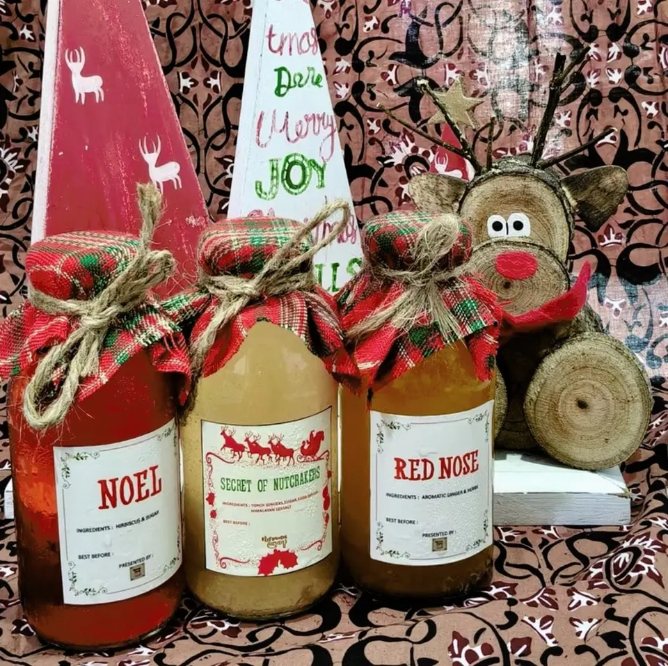 Tiga botol minuman Noel, Secret of Nutcrakers, dan Red Nose bertutup kain kotak merah hijau dengan hiasan Natal