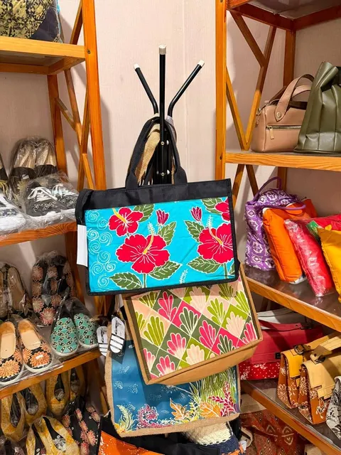Tas jinjing berpanel batik motif kembang sepatu merah tergantung di antara rak sepatu dan tas