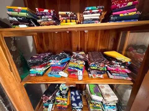 Tumpukan kain batik terlipat aneka warna di rak kayu berkaca