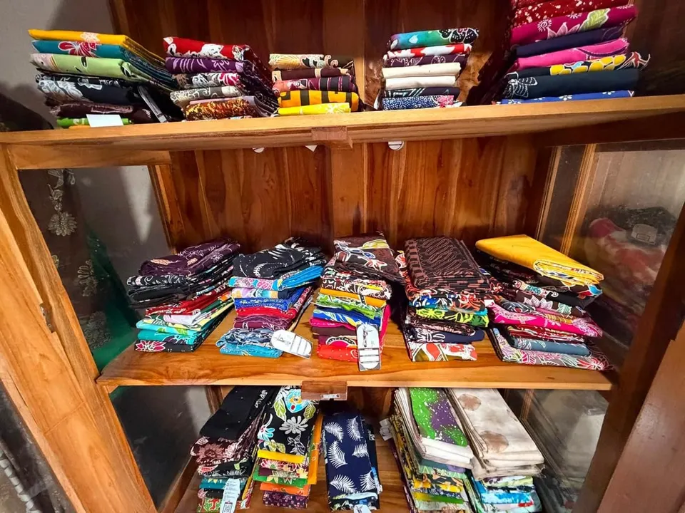 Tumpukan kain batik terlipat aneka warna di rak kayu berkaca