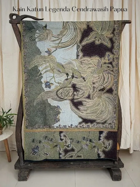 Kain batik bermotif burung cendrawasih warna hijau keabuan dan cokelat tergantung di gawangan kayu
