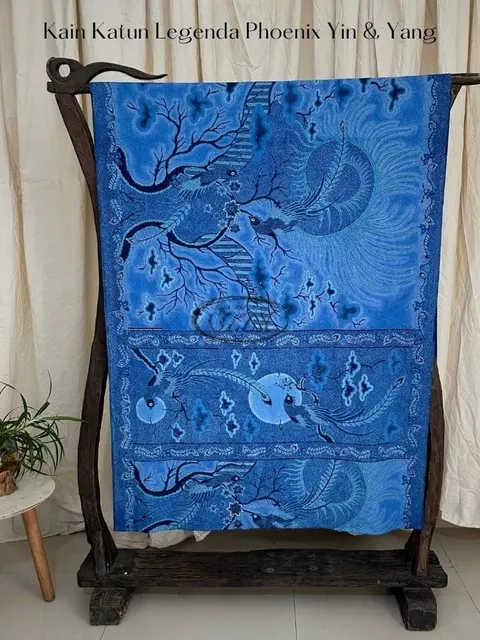 Kain batik biru bermotif burung phoenix tergantung di gawangan kayu di depan tirai krem