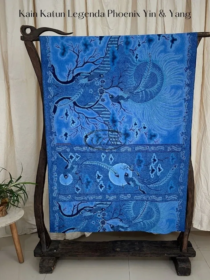 Kain batik biru bermotif burung phoenix tergantung di gawangan kayu di depan tirai krem