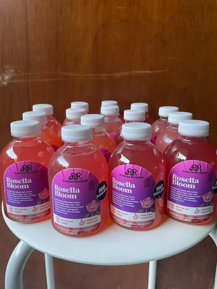 Belasan botol Rosella Bloom berisi minuman merah muda dengan label ungu tersusun di atas kursi putih