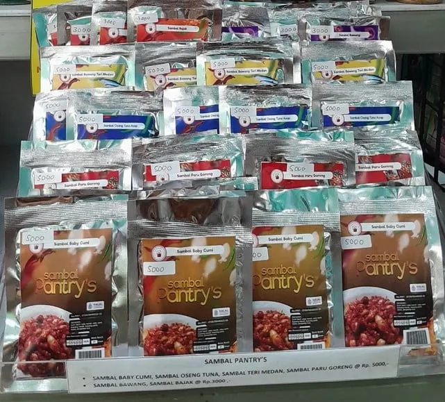 Rak berisi deretan sachet sambal Pantry's aneka varian berlabel harga dengan papan daftar harga di bawahnya