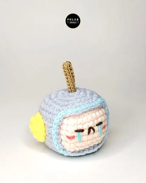 Boneka rajut kecil berbentuk kotak abu-abu dengan wajah menangis bersulam dan antena cokelat keemasan