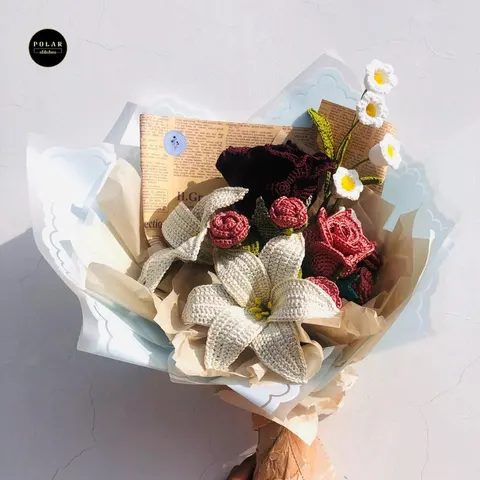 Buket bunga rajut berisi mawar merah, lili krem dan bunga putih kecil dibungkus kertas putih