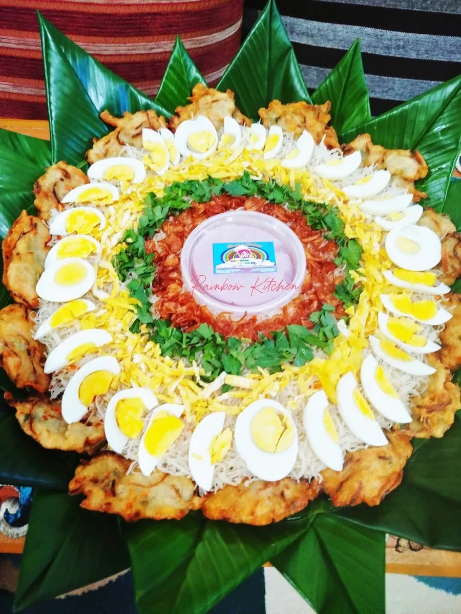 Bihun nampan beralas daun pisang berhias telur rebus, telur dadar iris, daun seledri dan gorengan di tepinya