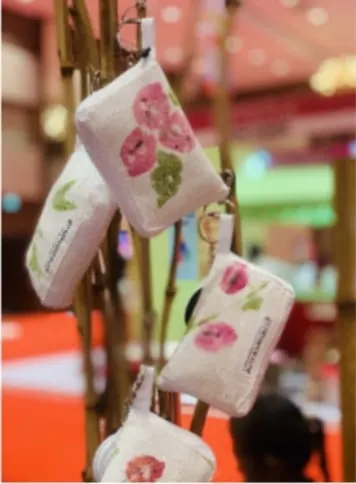Beberapa pouch kain putih bermotif cetak bunga merah muda dan daun hijau tergantung pada batang bambu