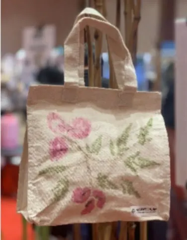 Tas jinjing kain putih bermotif cetak bunga merah muda dan daun hijau tergantung di stan pameran