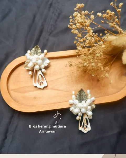 Dua bros kerang dan mutiara air tawar dengan daun keemasan di atas nampan kayu oval