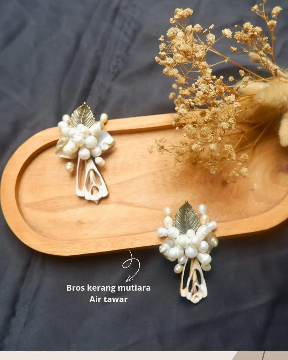 Dua bros kerang dan mutiara air tawar dengan daun keemasan di atas nampan kayu oval